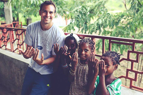 Andrew, a student, in Haiti with three other Haitian kids. They appear as though they are trying to signal the "U" sign.  