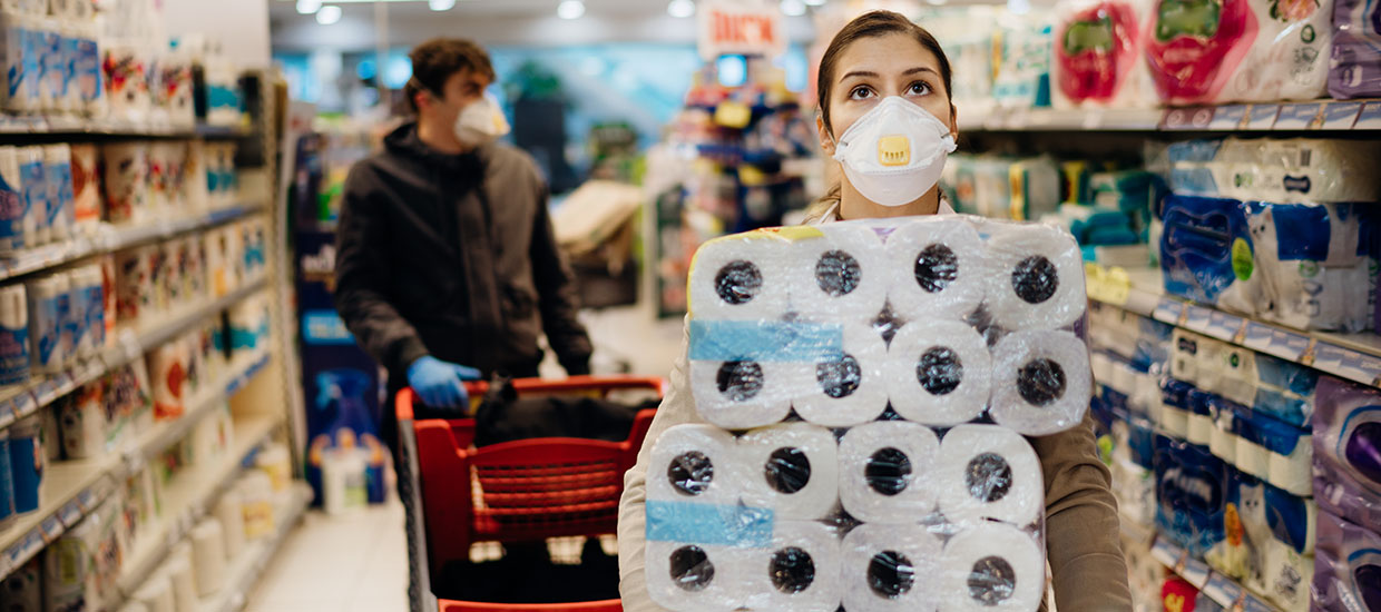 This is a stock photo. A man and a woman in a store shopping for toilet paper and wearing medical masks.