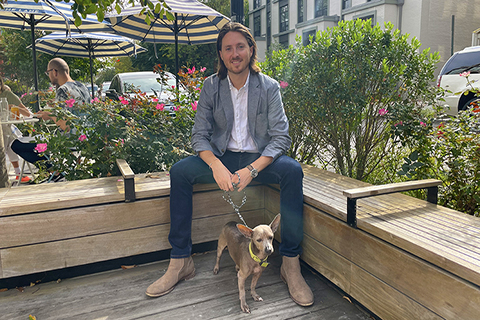 This is a photo of MAIA alumni, Jesse Kornbluth. Jesse is stilling outside on a bench with his dog.